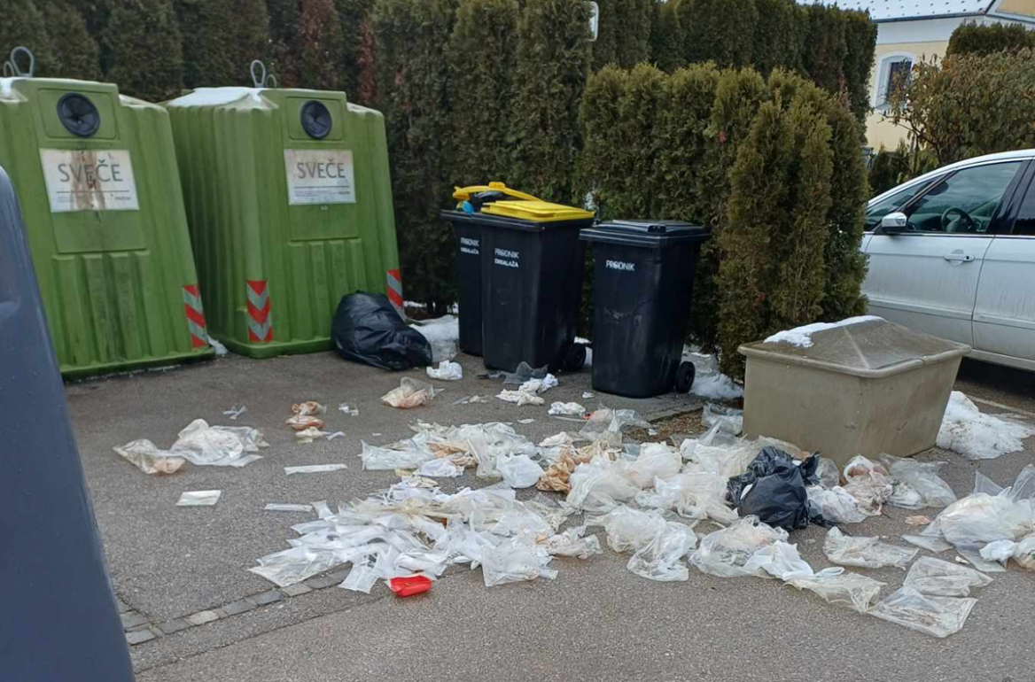 Dva zelena zabojnika za steklo, dva črna zabojnika z rumenim pokrovom in en črni zabojniki, pred njimi na tleh pa kup razmetanih prozornih umazanih plastičnih vrečk.